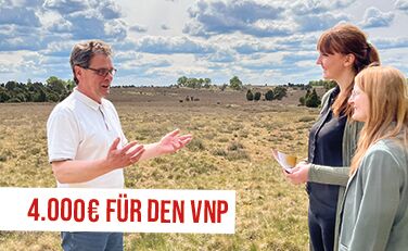 Steffen Albers (VNP) berichtet Lisa Persiel und Patrizia Jäger (Lünestrom) von den Pflegemaßnahmen der Heideflächen, davor Schriftzug "4.000€ für den VNP"