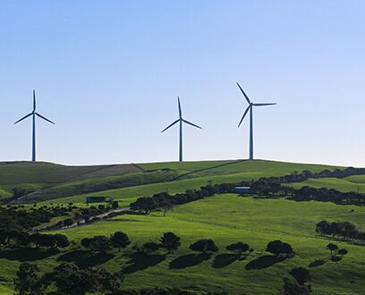 Drei Windräder am Horizont einer hügeligen Landschaft.