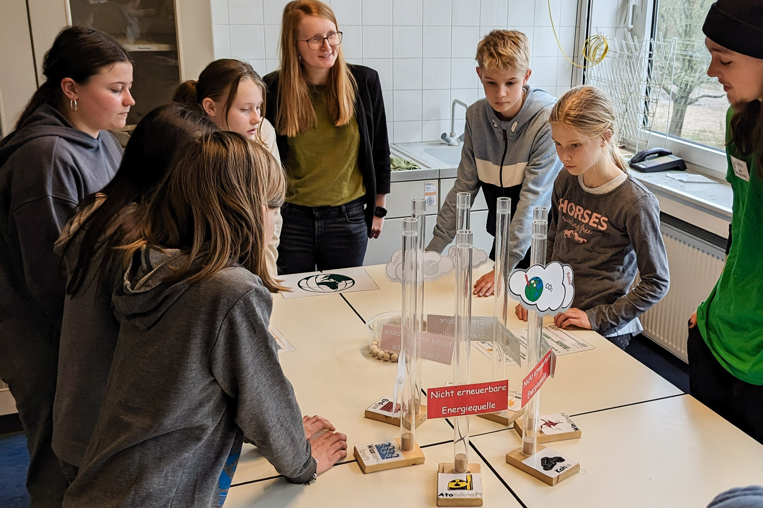 Sechs Schüler*innen betrachten gemeinsam mit einer Lünestrom-Mitarbeiterin und einem SCHUBZ-Mitarbeiter die Energiearten-Station.